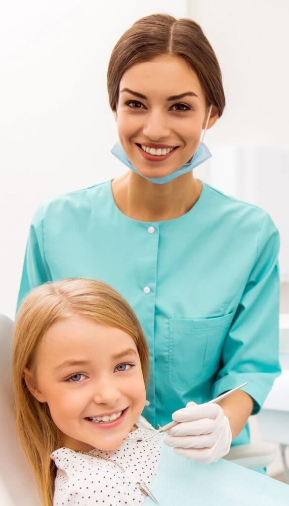 Smiling young patient seated in a dental chair in fron of a smiling dentist | Featured Image for the Dental Services Page of Restore Dental.