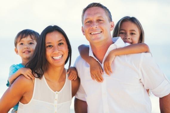 Smiling husband and wife each holding a child on thier backs | Featured Image for the Dental Services Page of Restore Dental.